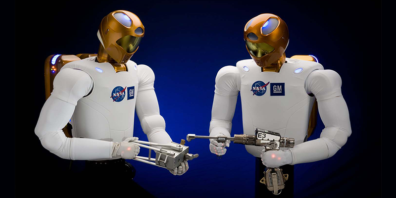 Two Robonaut humanoid robots facing each other holding space tools.