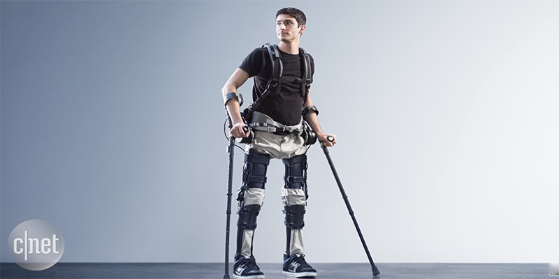 A person standing with the help of the Phoenix exoskeleton suit around their legs.