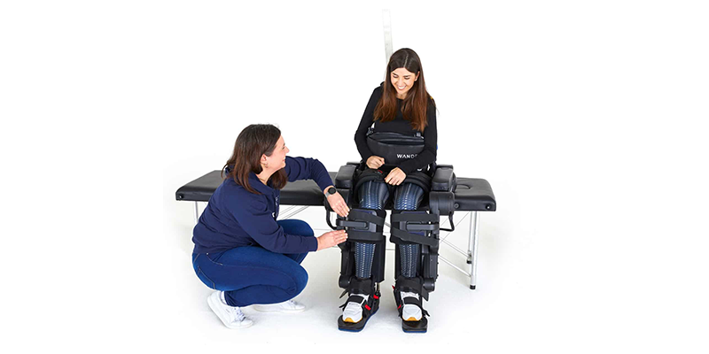 A person wearing the Alanlante X exoskeleton around their legs as a physical therapist assists them.