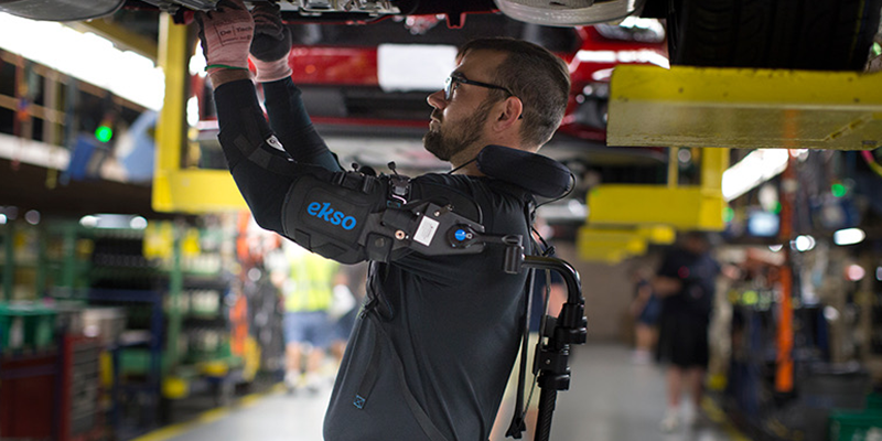 A person wearing the Esko Vest around their back and arms as they work on machinery overhead.