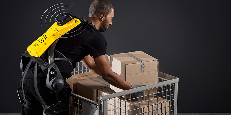 A person reaching down to lift boxes while wearing the Cray X exoskeleton suit with a signal coming off of it.