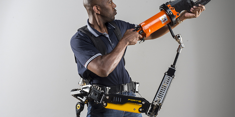 A person carrying heavy equipment with the help pf the Fortis exoskeleton suit around their waist.